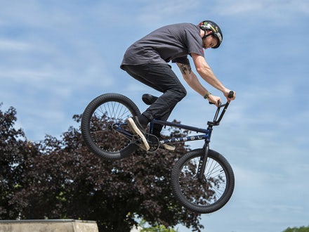 A BMX rider performing an aerial trick on the Huffy Symbol bike at a skatepark, with trees and a blue sky in the background. A BMX rider performing an aerial trick on the Huffy Symbol bike at a skatepark, with trees and a blue sky in the background.