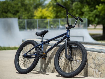 The Huffy Symbol BMX bike resting against a concrete ramp at a skatepark, with greenery and skate ramps in the background. The Huffy Symbol BMX bike resting against a concrete ramp at a skatepark, with greenery and skate ramps in the background.