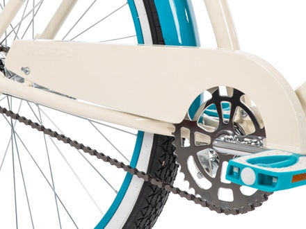 Close-up of a bike’s steel chain guard, crank, and teal pedal, highlighting smooth pedaling and stylish details.